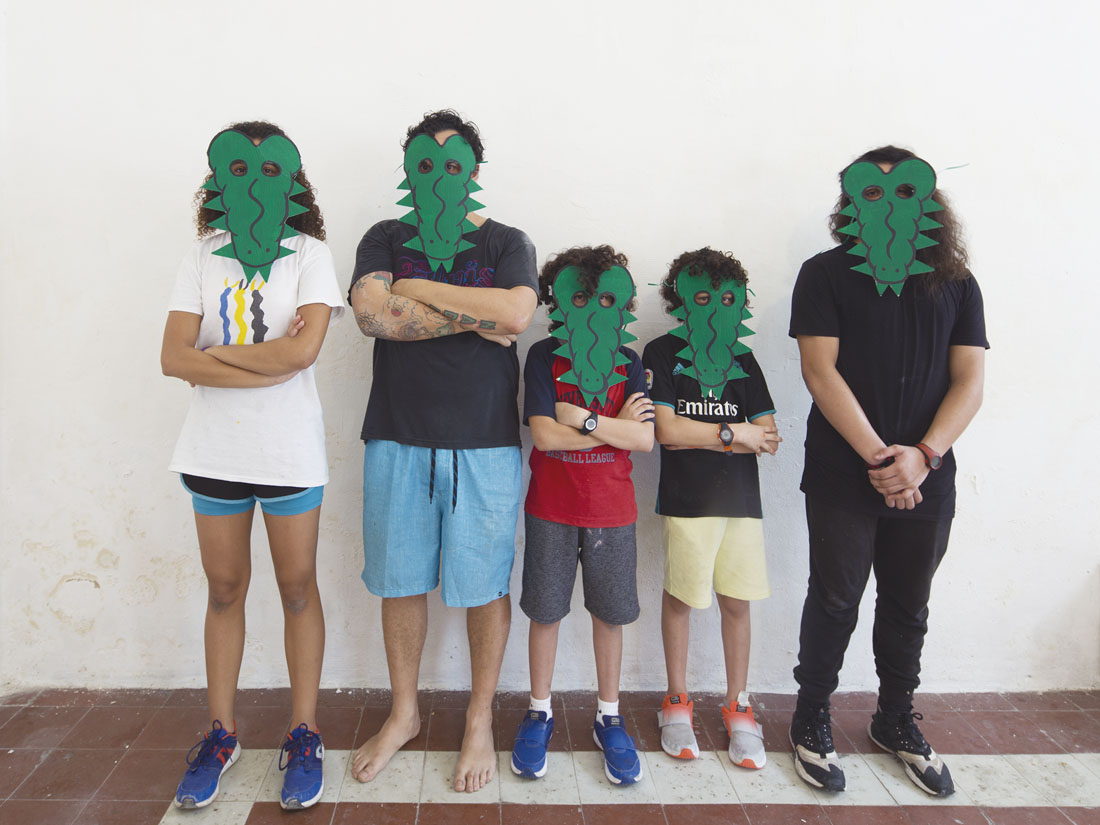 Fotografía de cinco personas de distintas edades de pie, con los brazos cruzados usando máscaras de cocodrilo.